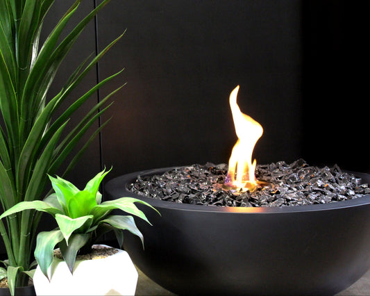 Fire pit with flames next to potted plants against a black background