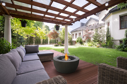 Outdoor patio with gray sectional sofa, wicker chairs, and fire pit under a wooden pergola.
