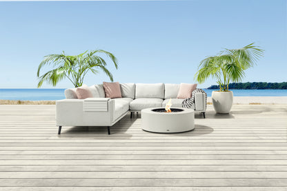 Outdoor patio set with sectional sofa, fire pit, and plants on a wooden deck by the water.