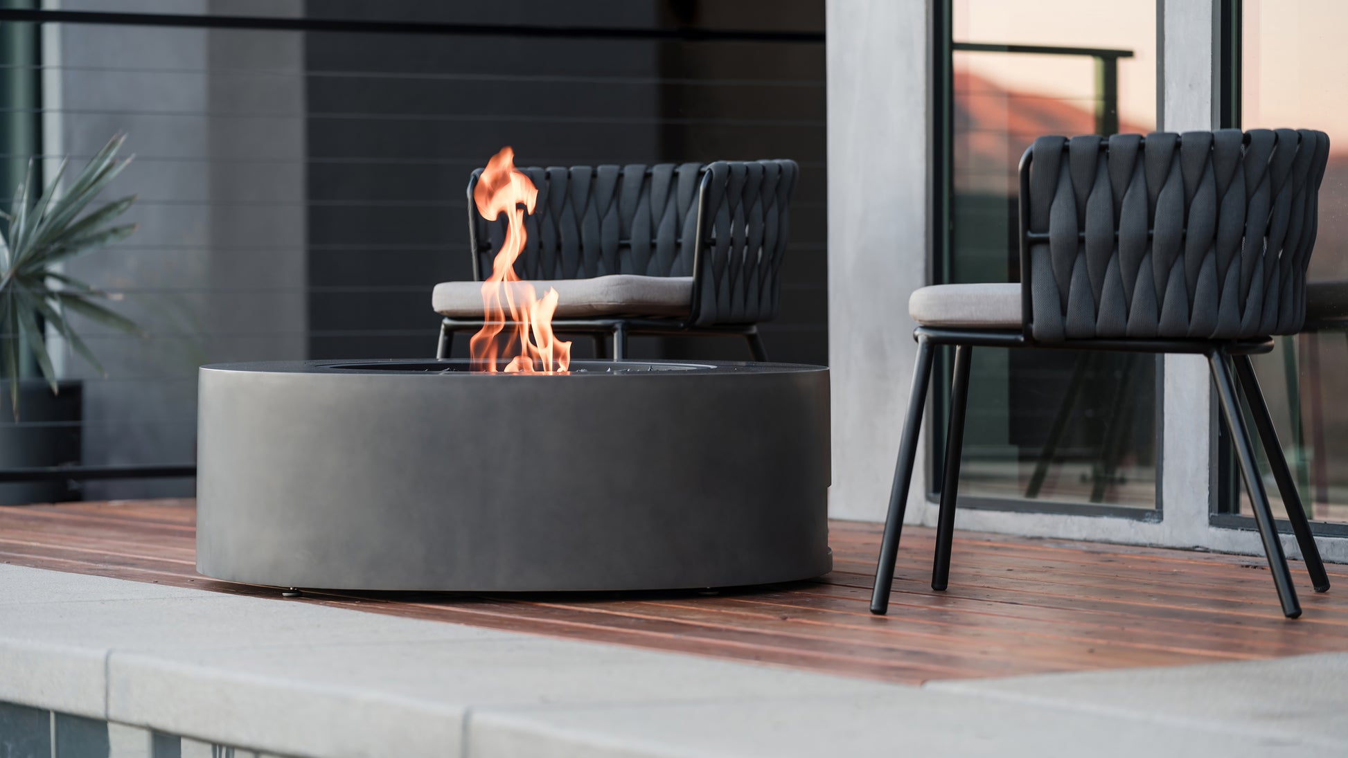 Fire pit table with flames on a patio area with chairs and a building in the background