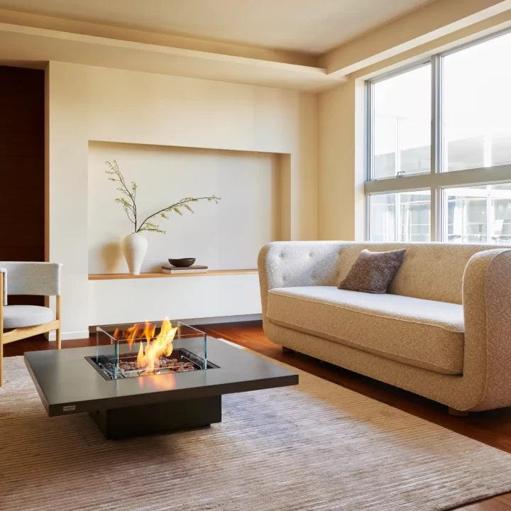 Modern living room with a fire pit table, beige sofa, and large window.