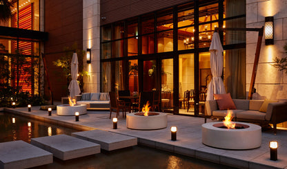 Evening outdoor setting with fire pits, seating areas, and illuminated building facade.