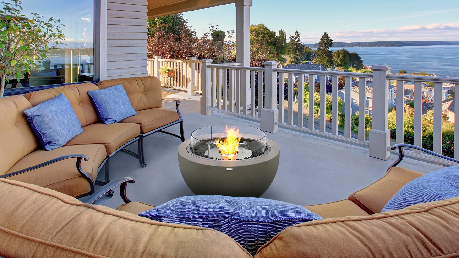 Outdoor patio with beige sofa, blue pillows, and fire pit overlooking a scenic view.