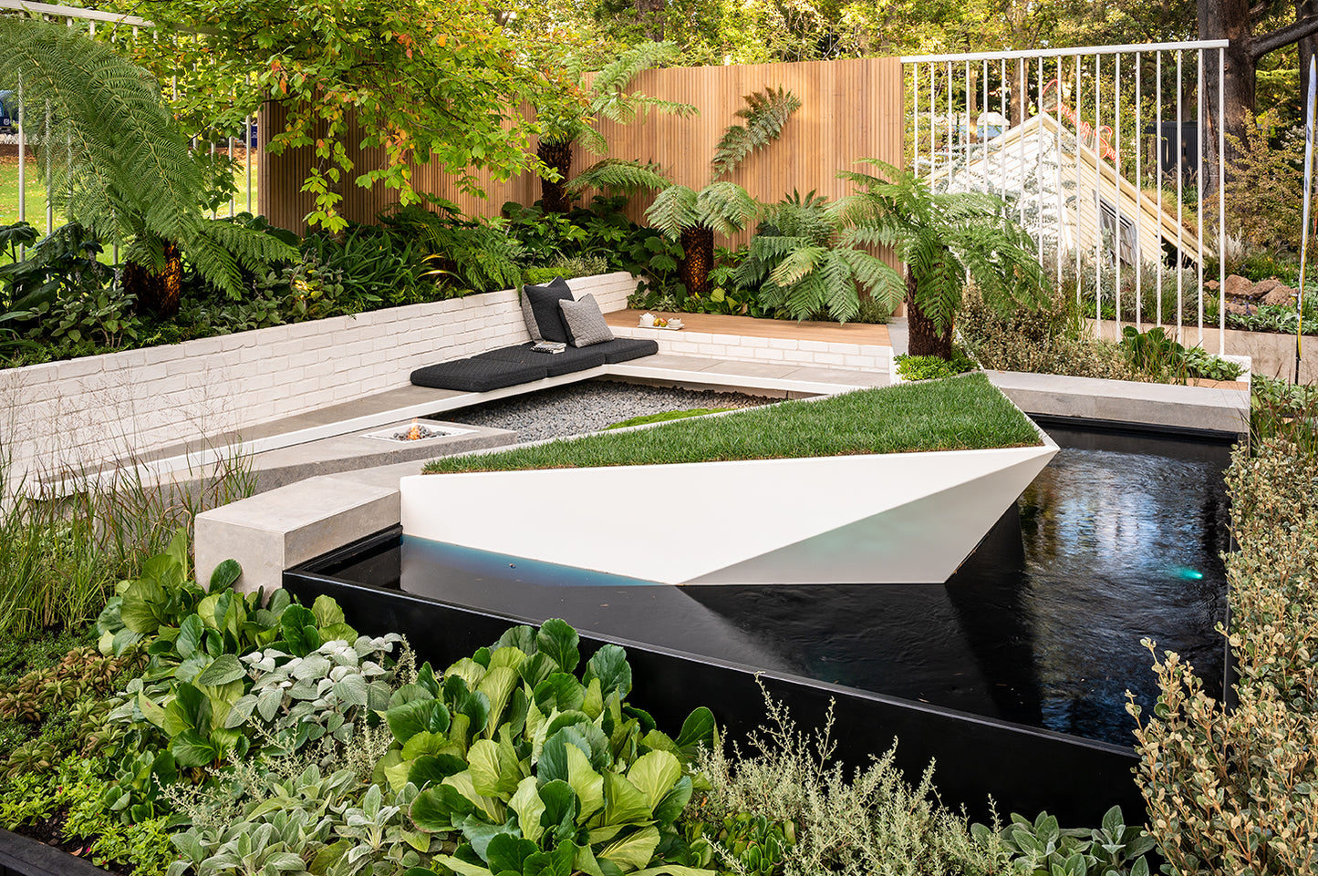 Modern garden with a water feature, seating area, and lush greenery.