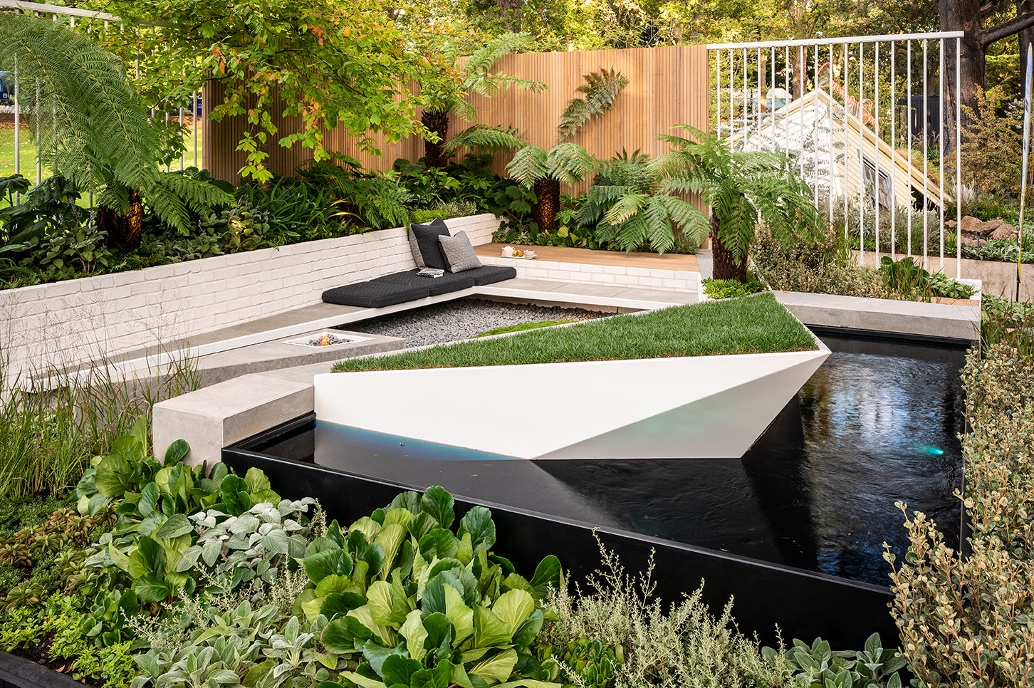 Modern garden with a water feature, seating area, and lush greenery.