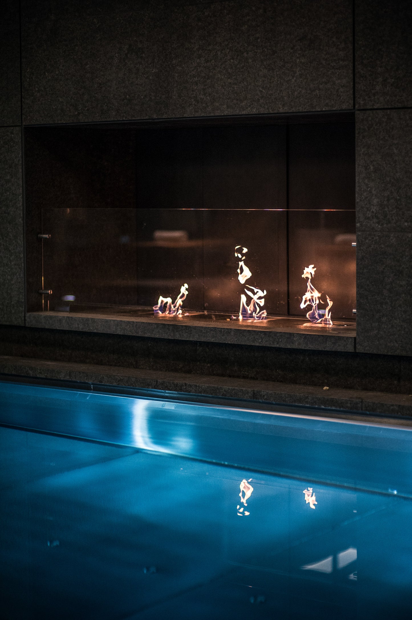 Fireplace with decorative metal figures inside, reflecting on a blue surface below.