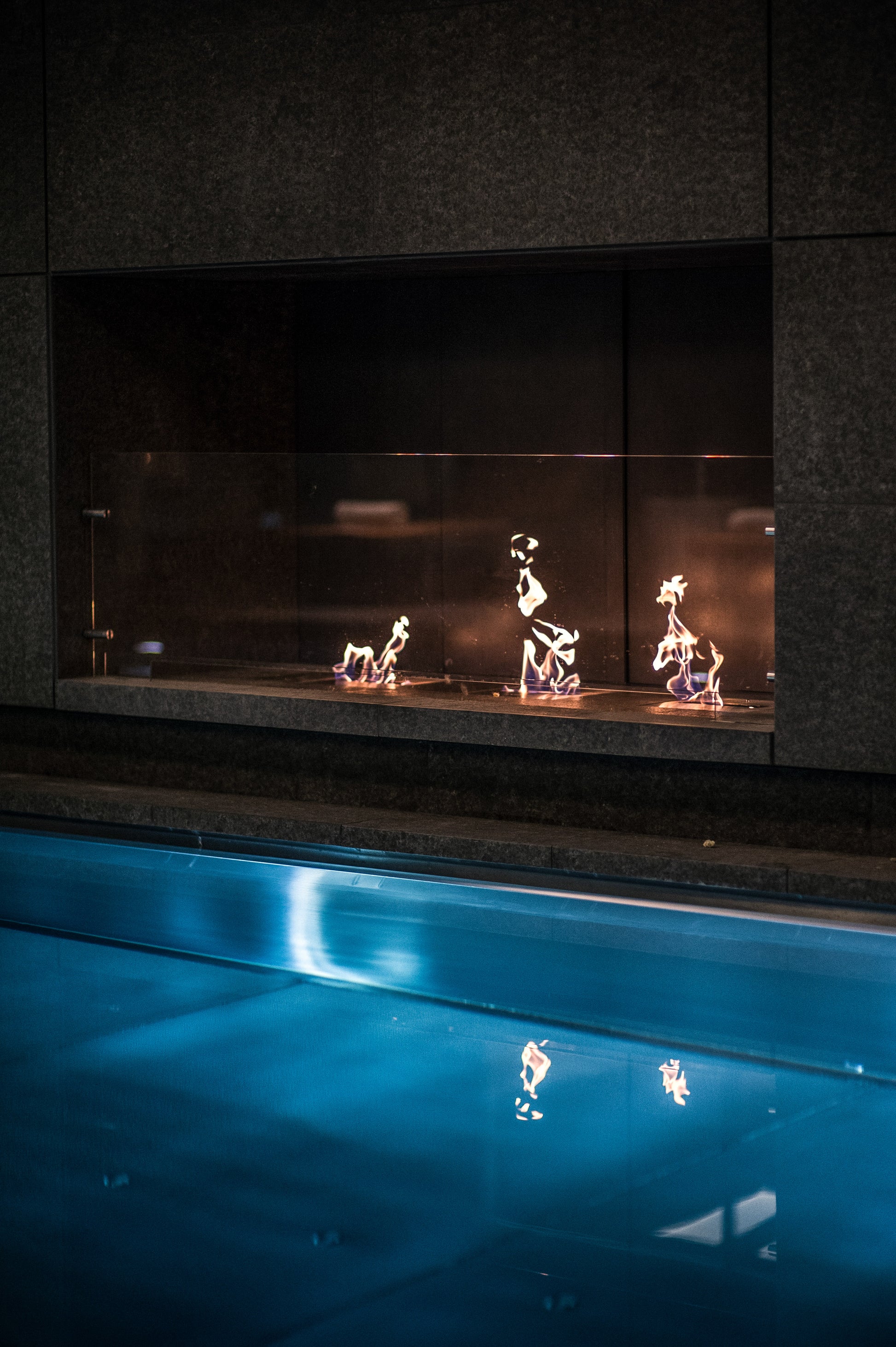 Fireplace with decorative metal figures inside, reflecting on a blue surface below.