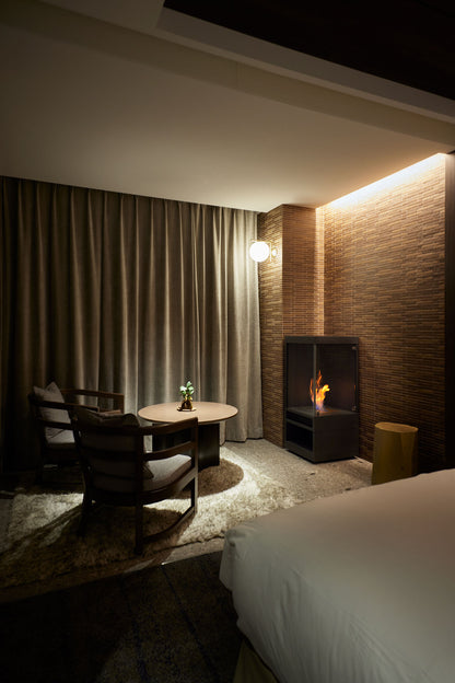 Modern bedroom with a bed, table, chairs, and a fireplace.