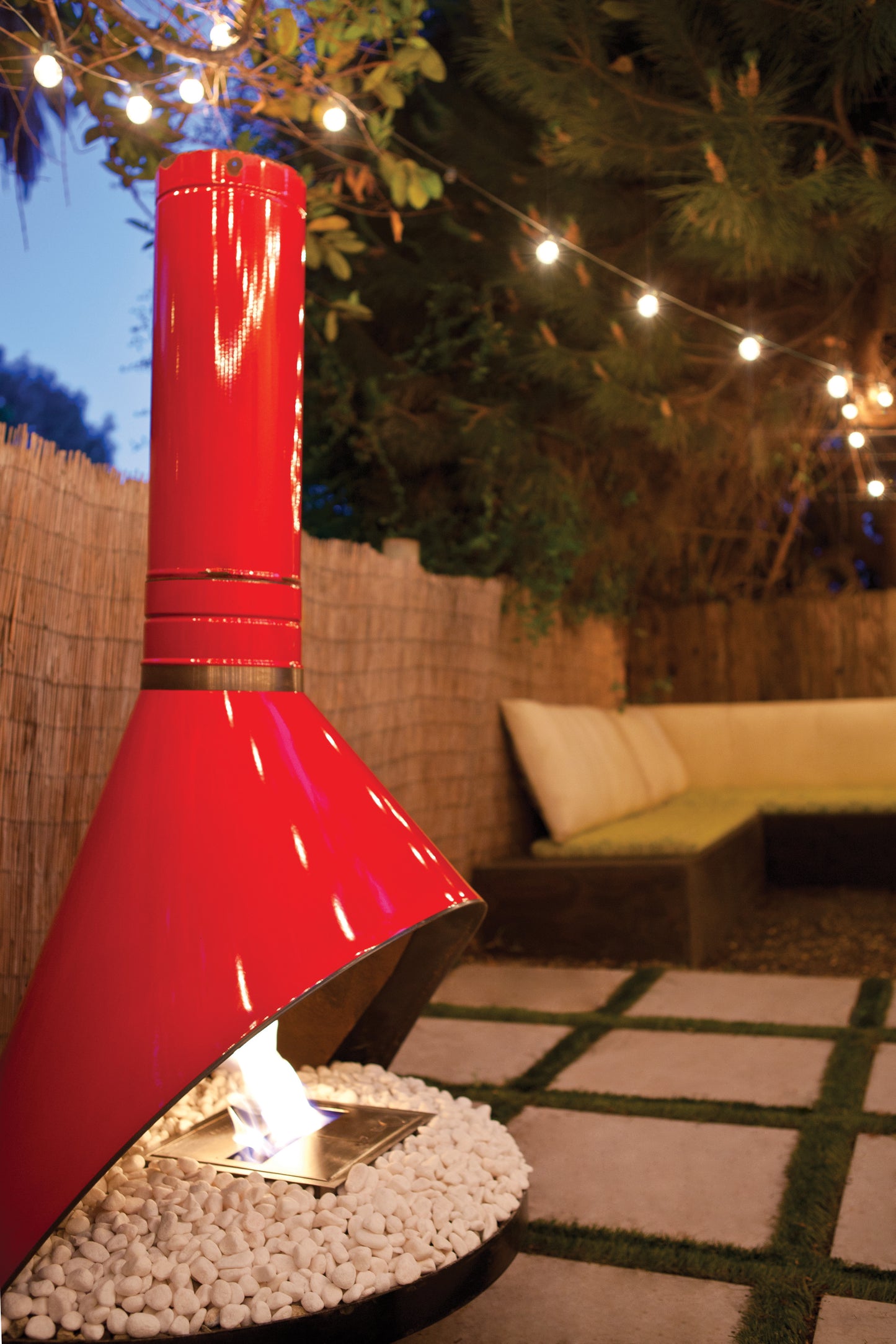Red outdoor fireplace with a garden setting and string lights.