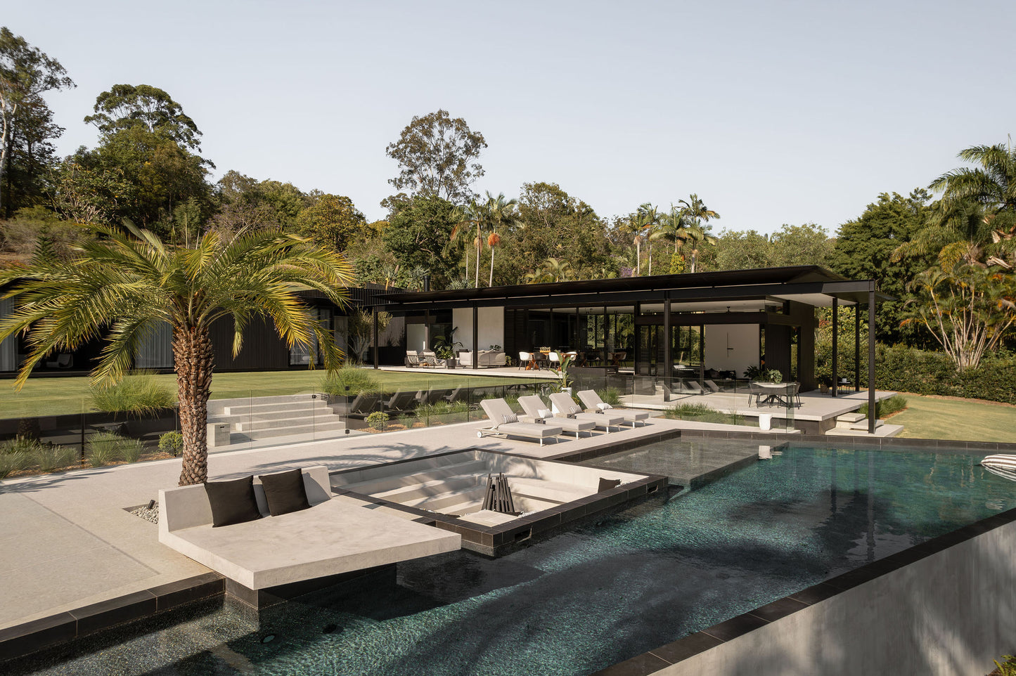 Modern outdoor living area with pool, lounge chairs, and covered pavilion.