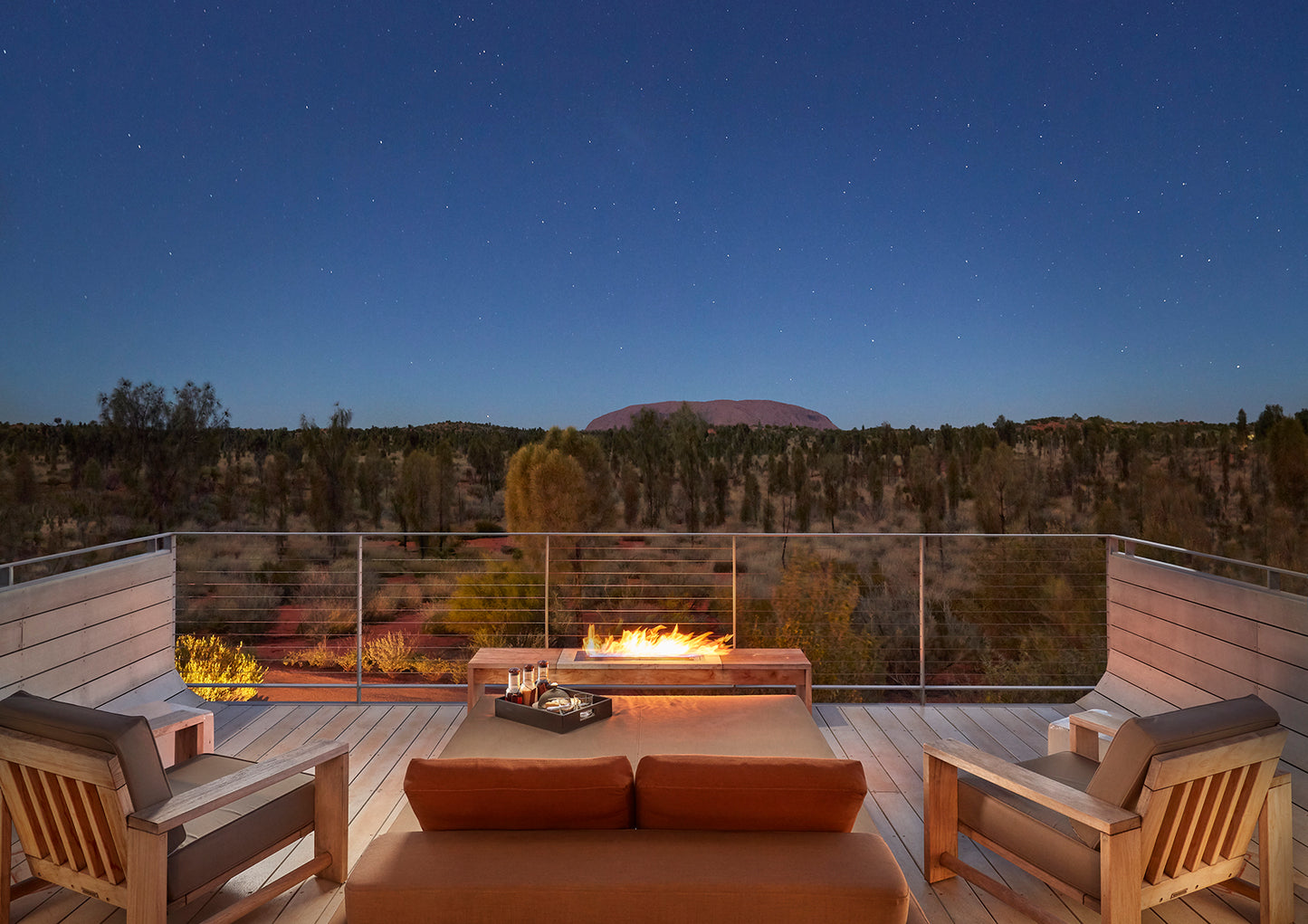 Outdoor deck with fire pit and seating area at night, Uluru visible in the background