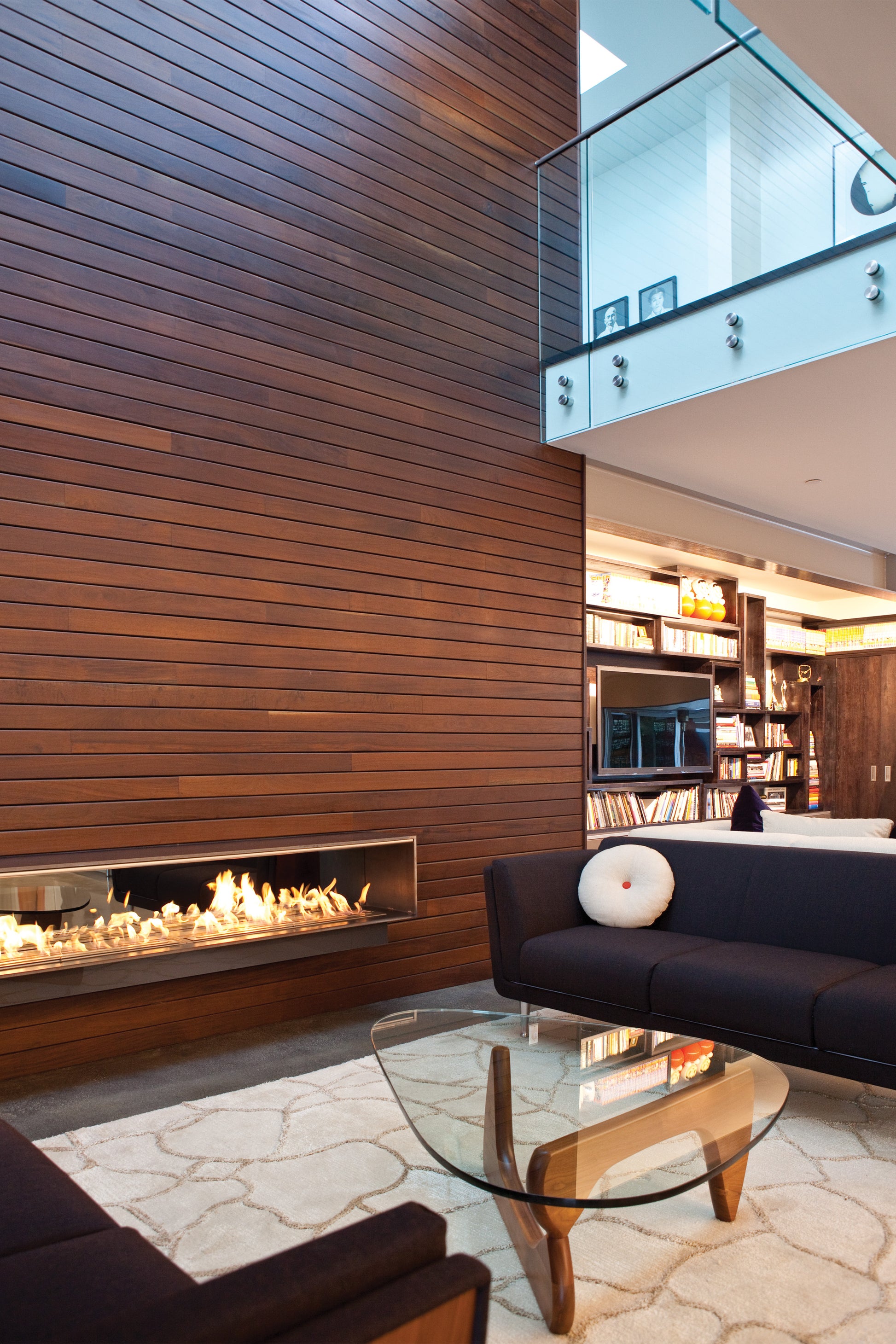 Modern living room with wooden wall, fireplace, and black sofa.