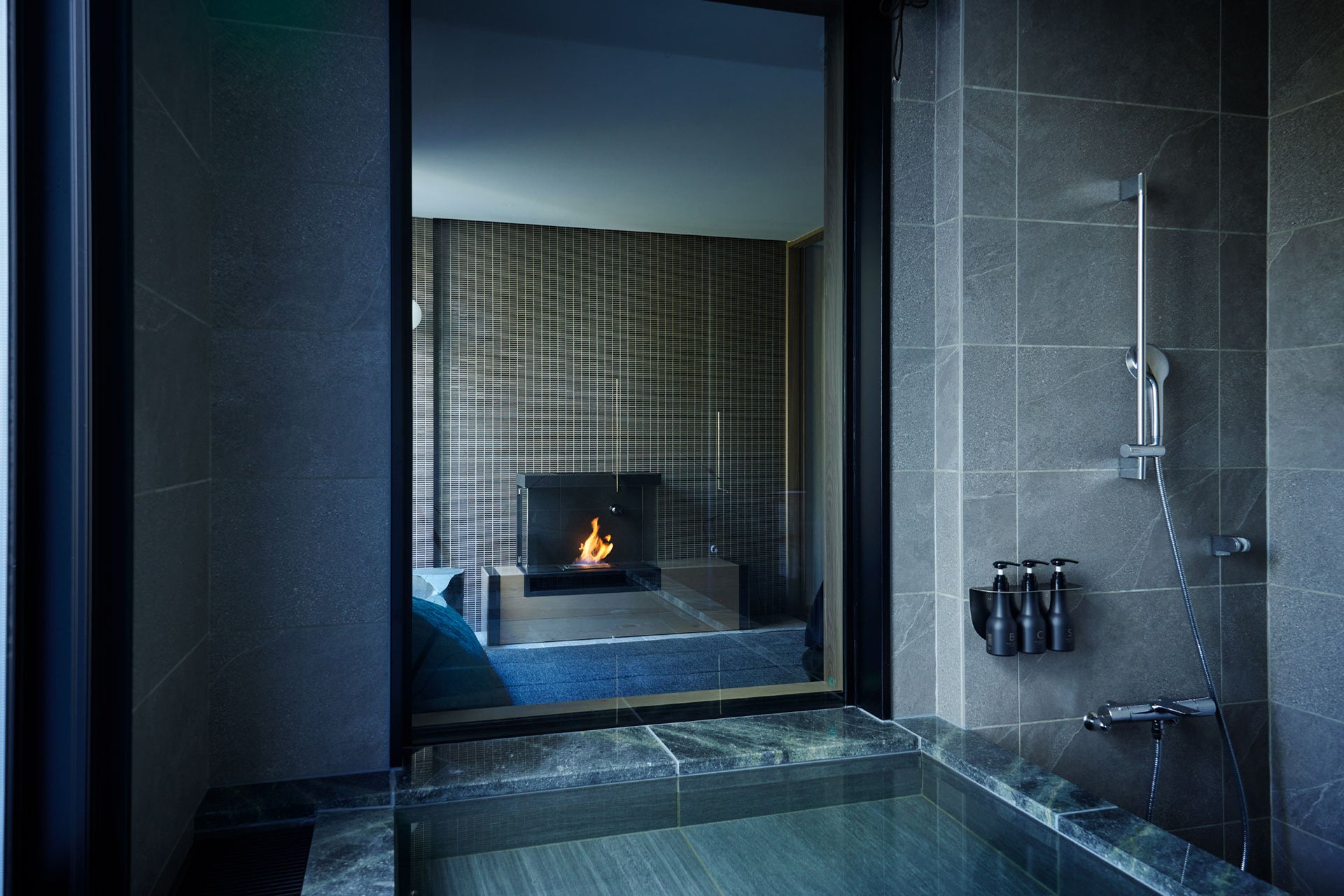 Modern bathroom with a fireplace visible through a glass wall.