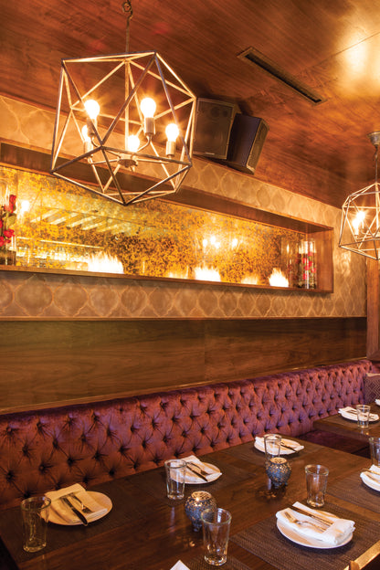 Dining area with wooden tables, purple velvet booths, and geometric chandeliers.