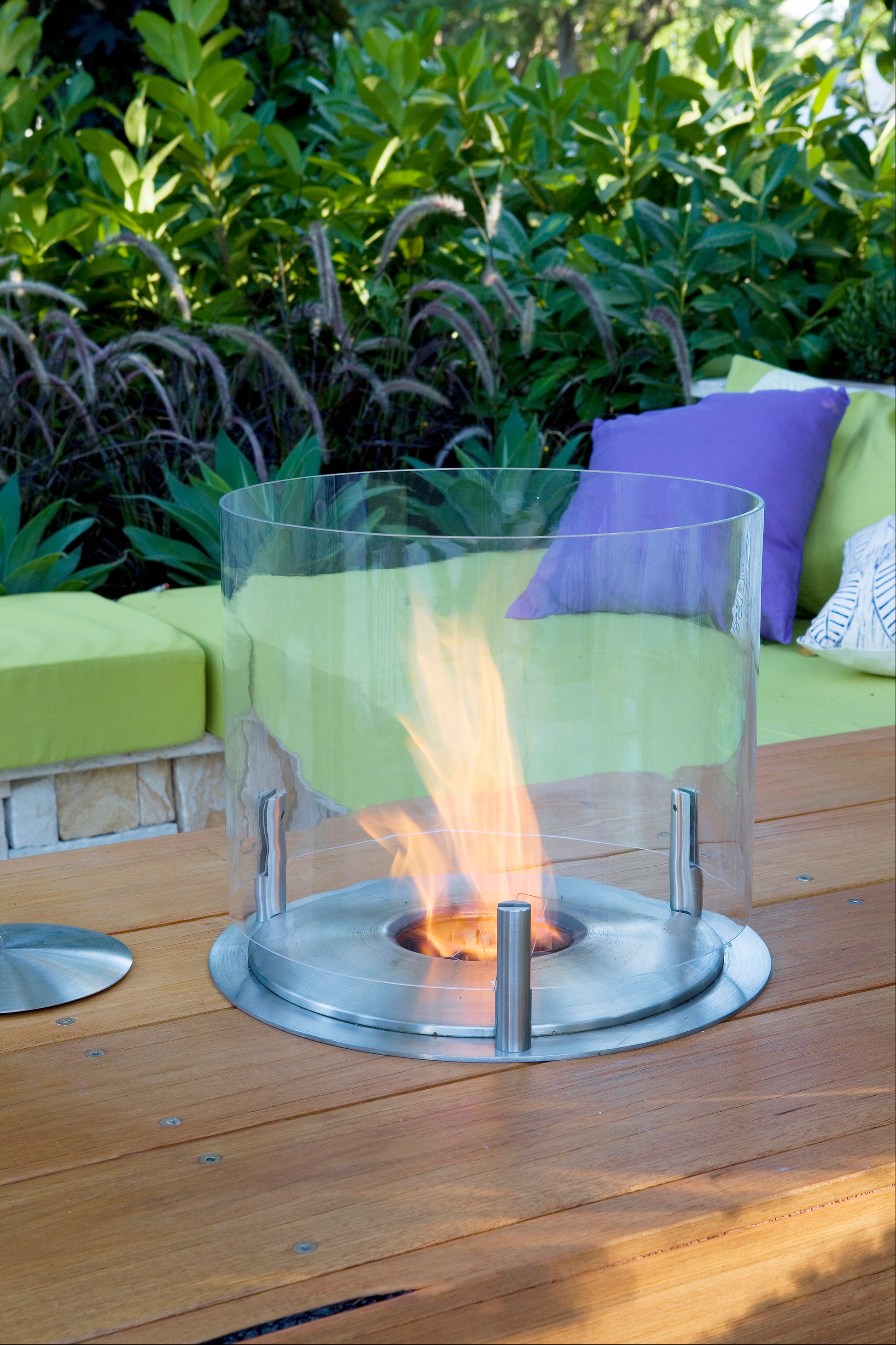 Outdoor fire pit on a wooden deck with green and purple cushions in the background