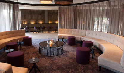Modern lounge area with curved beige sofas, purple ottomans, and a fire pit table.