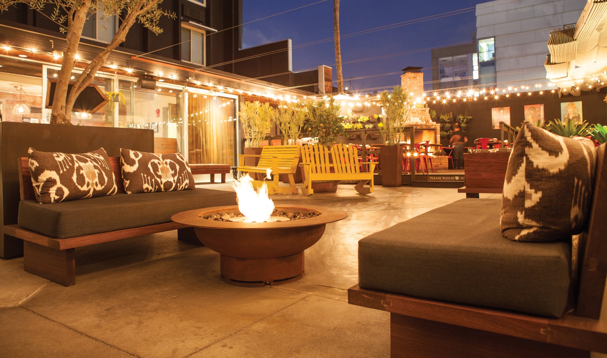 Outdoor patio area with fire pit, couches, and string lights at night.