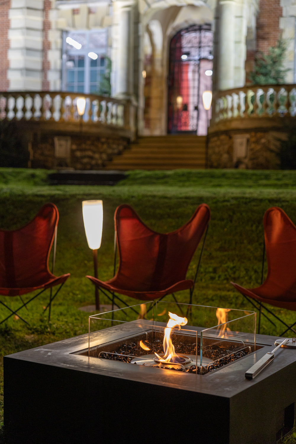 Fire pit with red chairs in a garden setting at night.