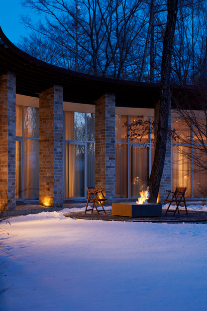 Modern house exterior with a fire pit and chairs in a snowy landscape