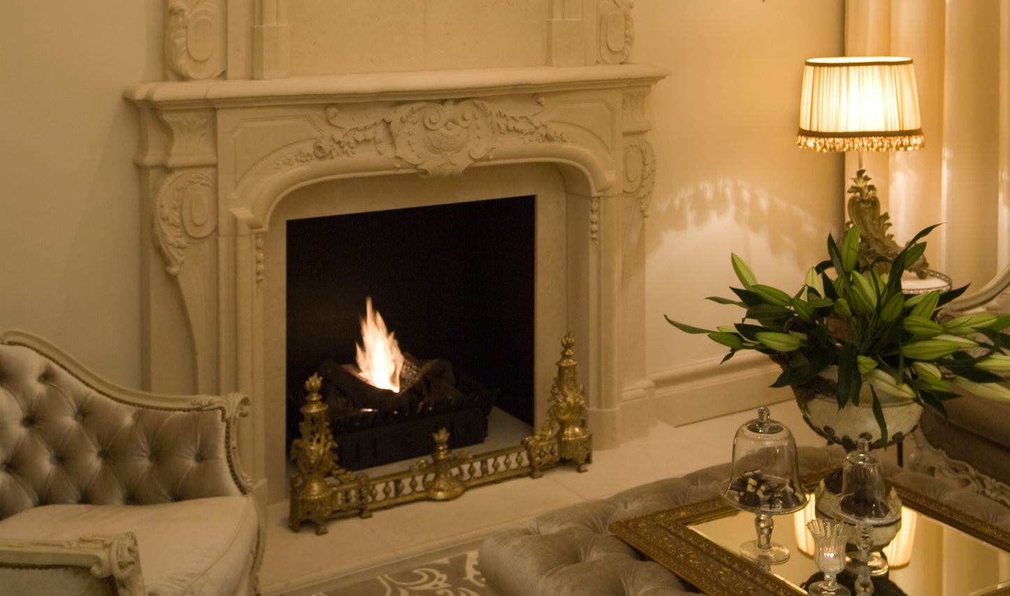 Decorative fireplace with ornate mantlepiece in a room with a lamp and plant.
