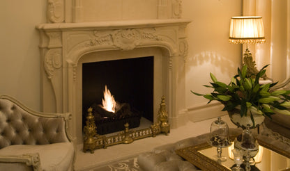 Decorative fireplace with ornate mantlepiece in a room with a lamp and plant.