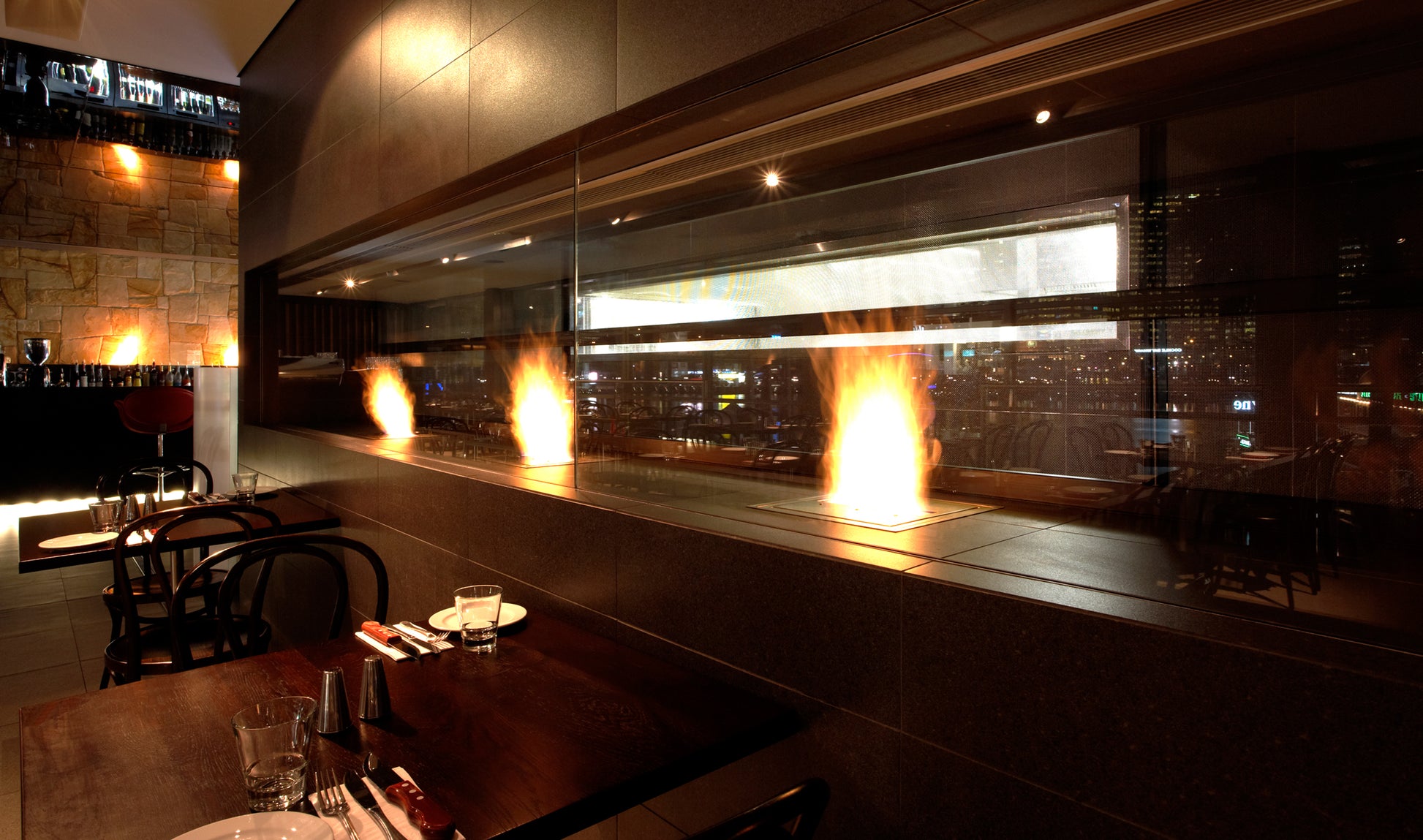 Modern restaurant interior with a long glass wall displaying flames.