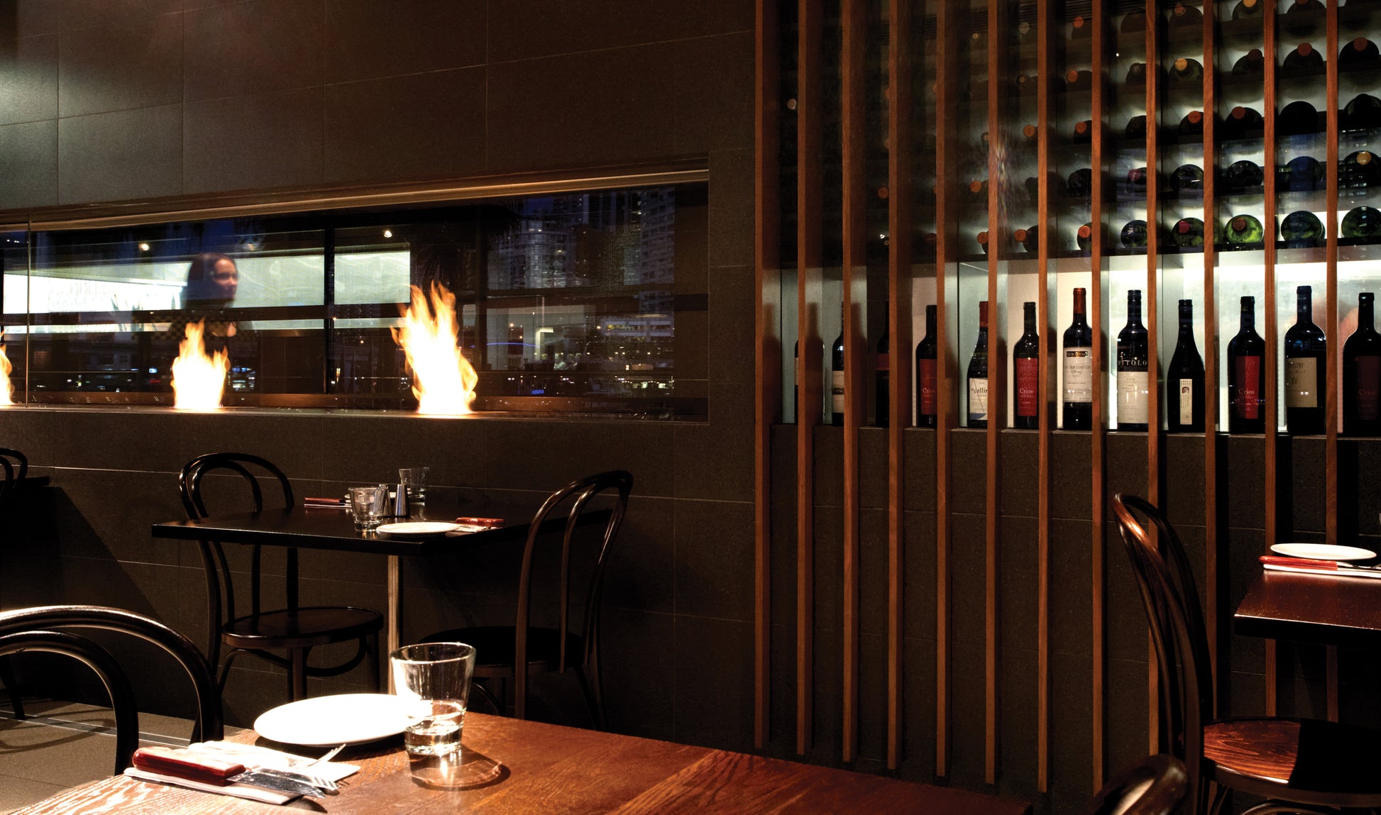 Dining area with wine bottles on a wall, table setting, and fireplace.