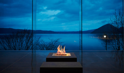 Fire pit by a large window with a view of a lake at night