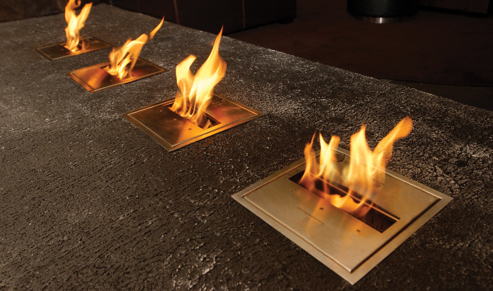 Four square fire pits with flames on a dark stone surface