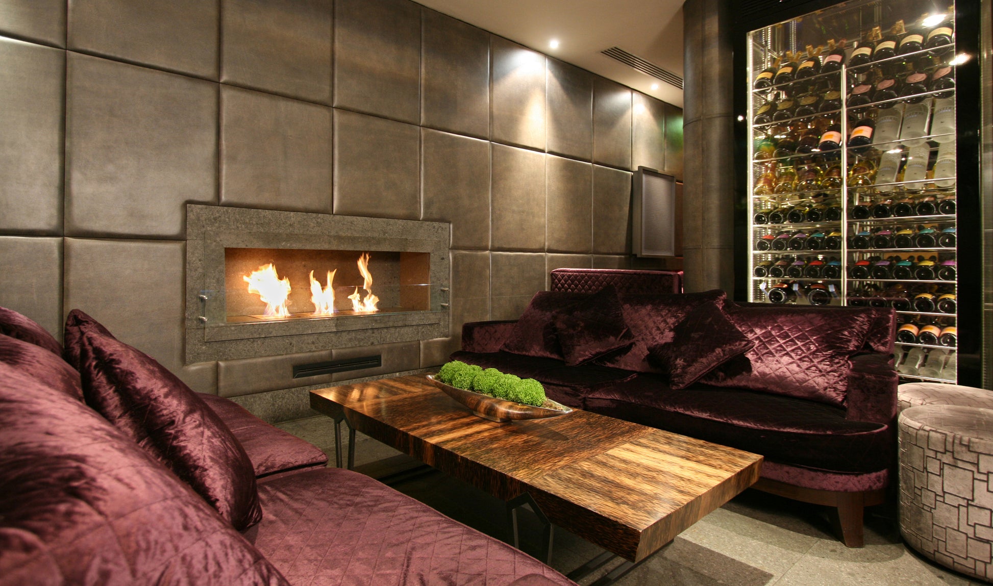 Modern living room with a fireplace, purple couches, and a wine rack.