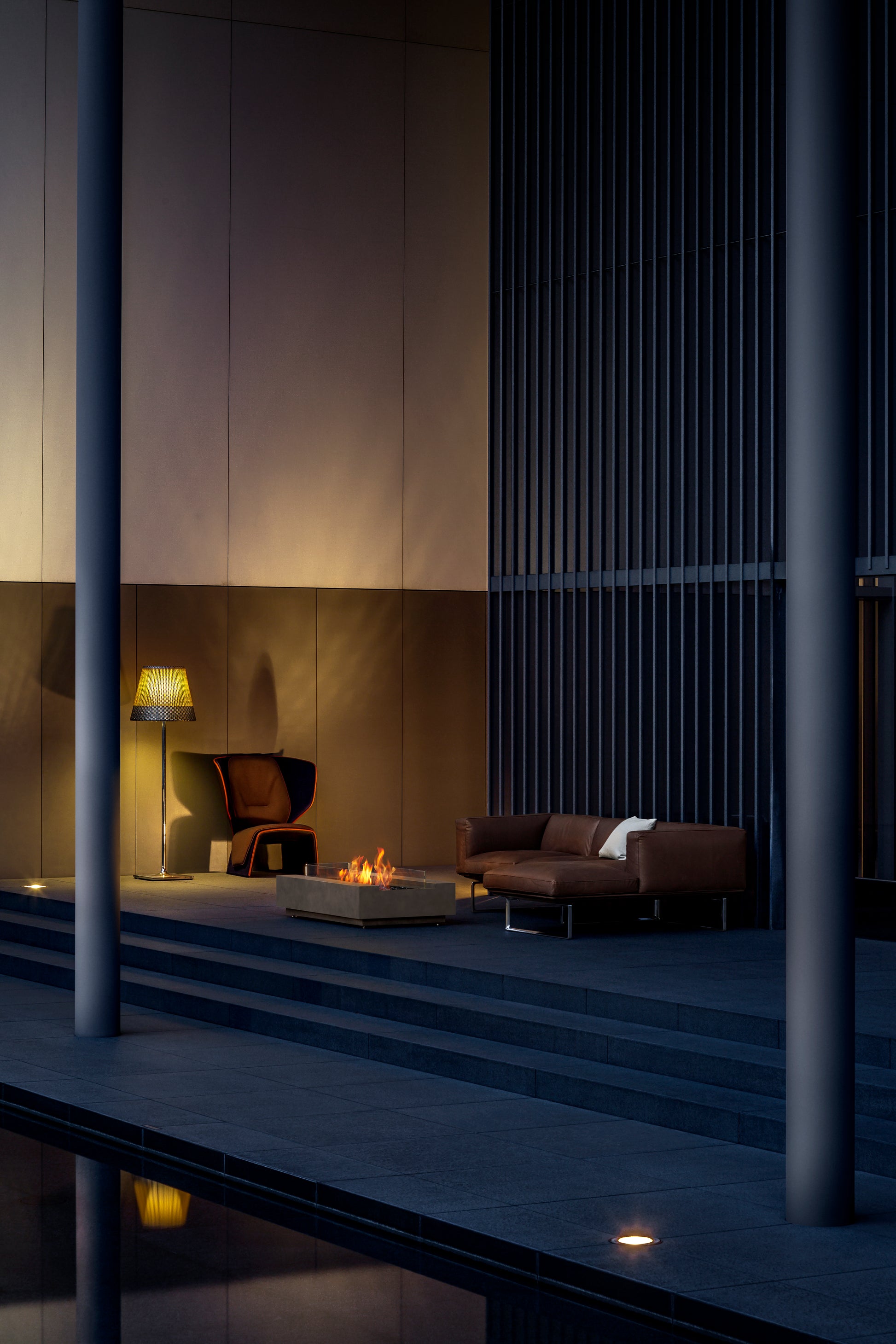 Modern indoor setting with a fire pit, sofa, and decorative lamp in a dimly lit room.