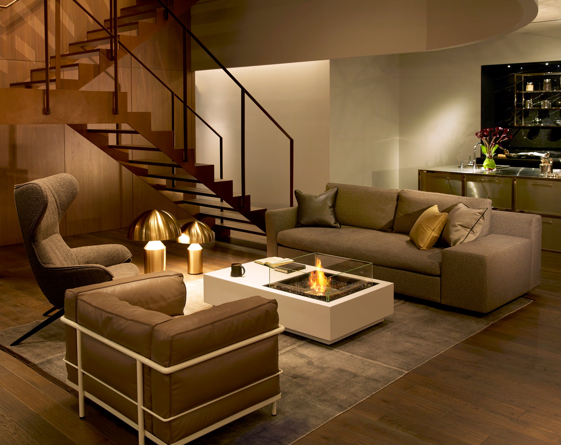 Modern living room with a staircase, sofa, and coffee table with a firepit.