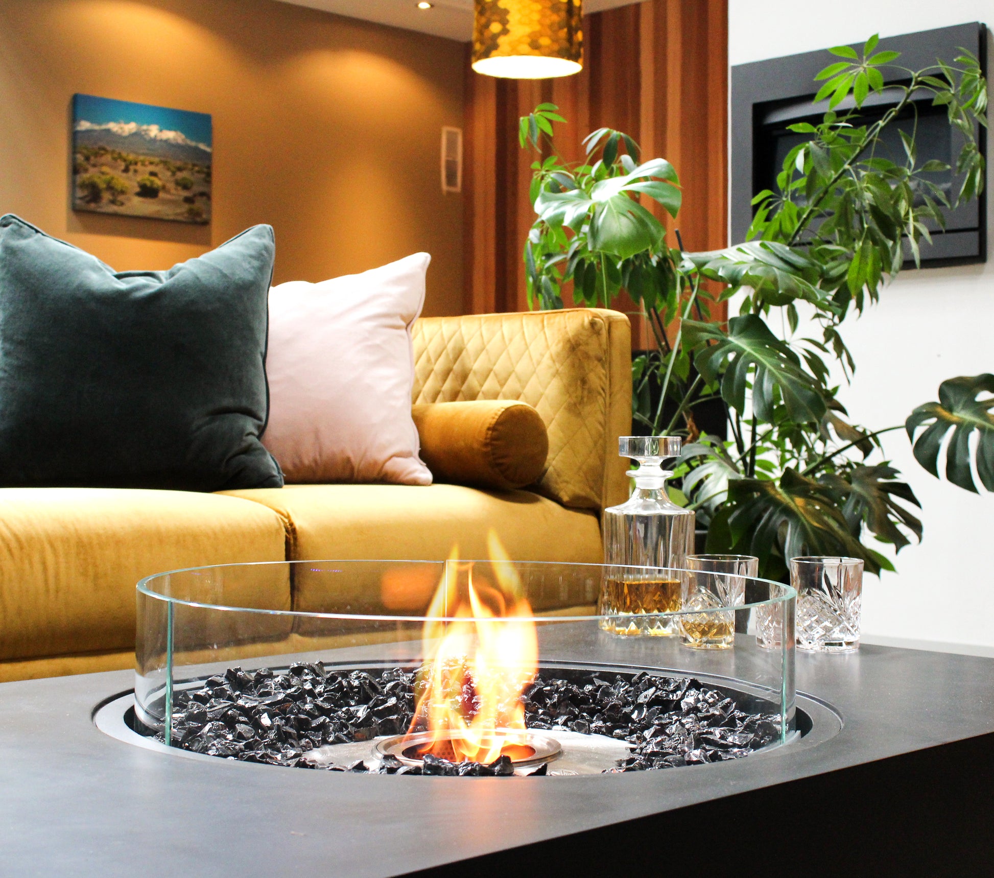 Modern living room with a fire pit table, yellow sofa, and decorative plants.