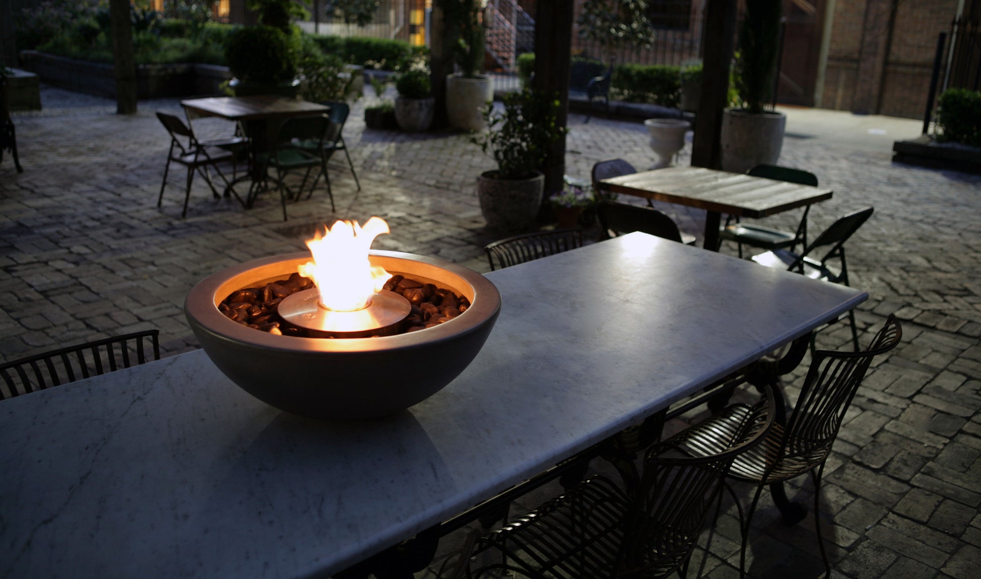 Fire pit on a table in an outdoor setting with chairs and tables around