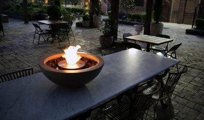 Fire pit on a table in an outdoor setting with chairs and tables around