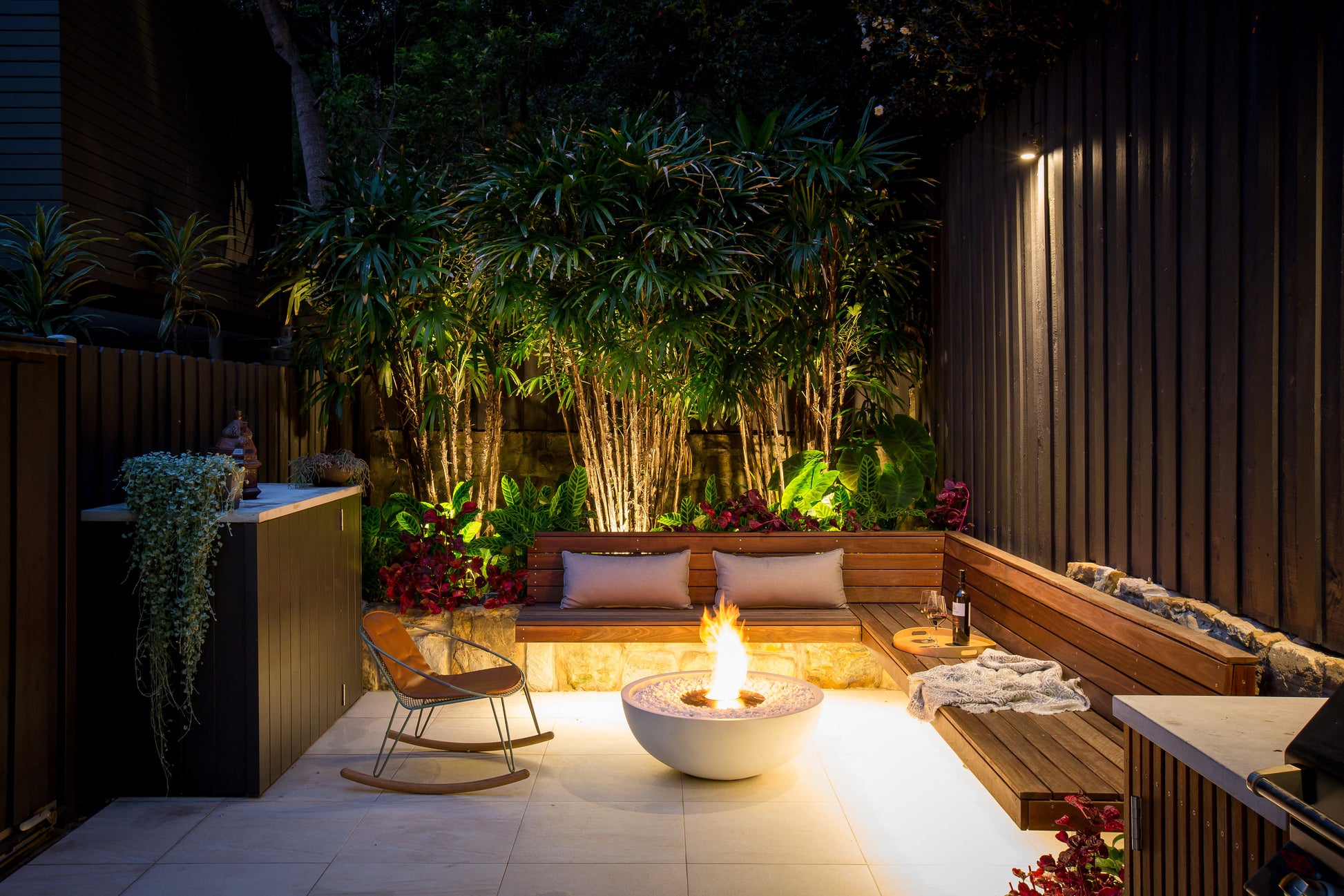 Outdoor patio with fire pit, chairs, and plants at night