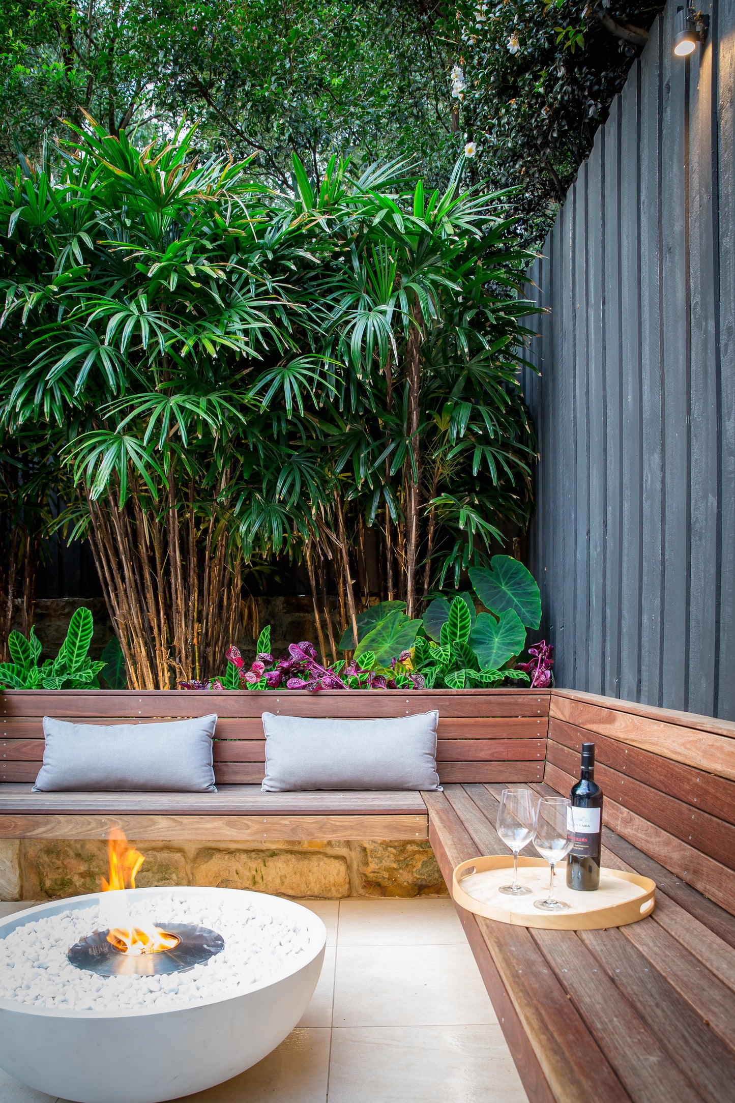Outdoor seating area with a fire pit, wine glasses, and a bottle in a garden setting.