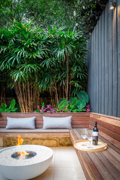 Outdoor seating area with a fire pit, wine glasses, and a bottle in a garden setting.