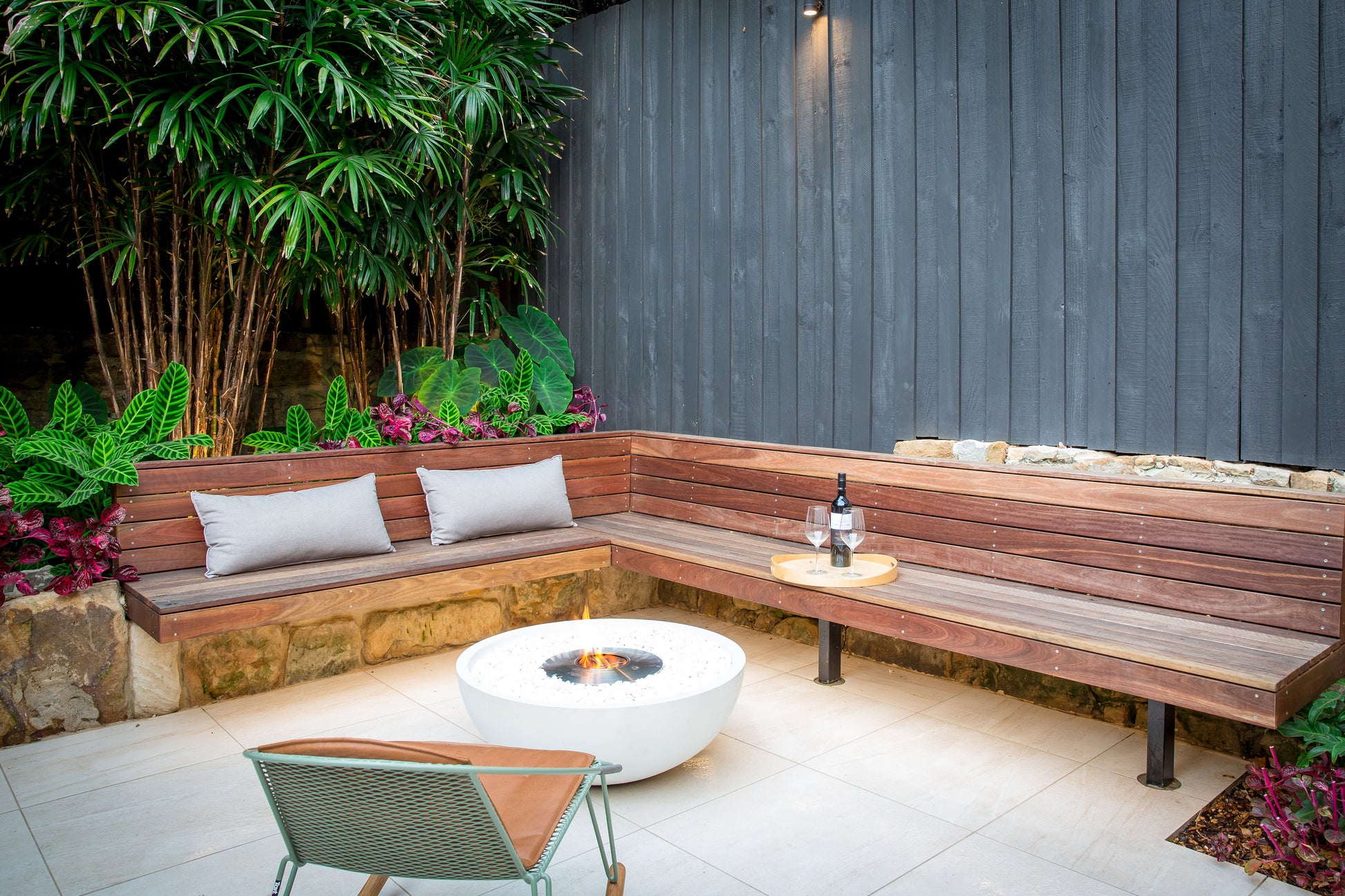 Outdoor seating area with wooden bench, fire pit, and plants.