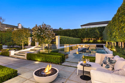Outdoor patio with fire pit, seating area, and pool in a well-maintained garden.