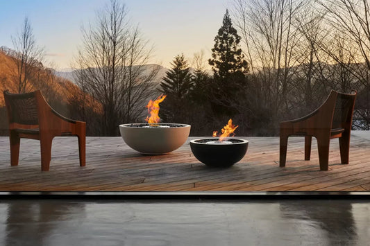 Two wooden chairs around two fire pits on a wooden deck with a scenic background.