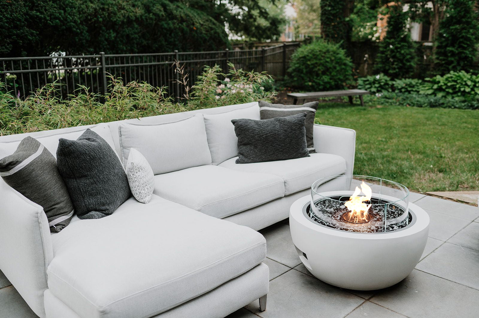 White outdoor sofa with gray and white pillows near a fire pit table on a patio.