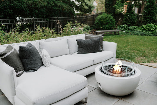White outdoor sofa with gray and white pillows near a fire pit table on a patio.
