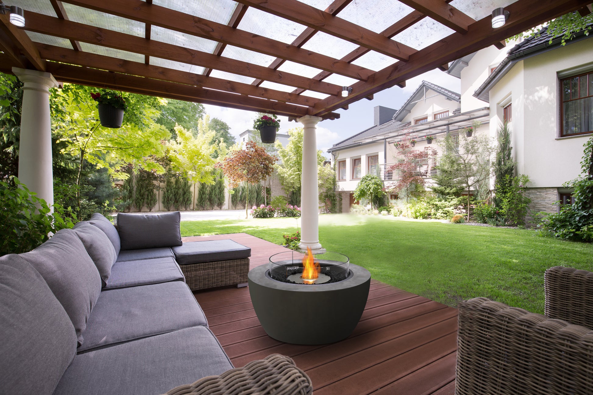 Outdoor patio with gray sectional sofa, wicker chairs, and fire pit under a wooden pergola.