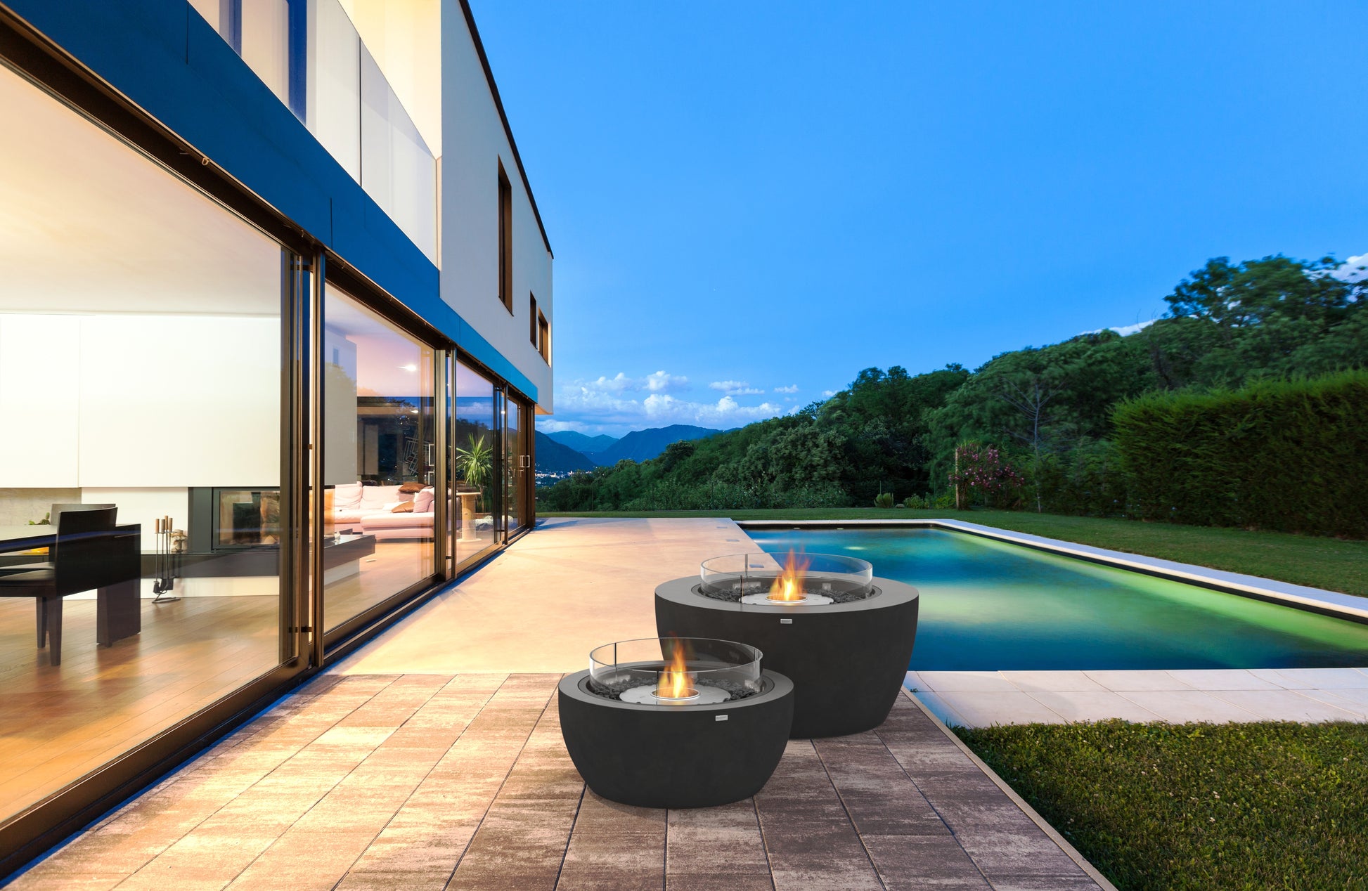 Modern house exterior with fire pits by a pool at dusk