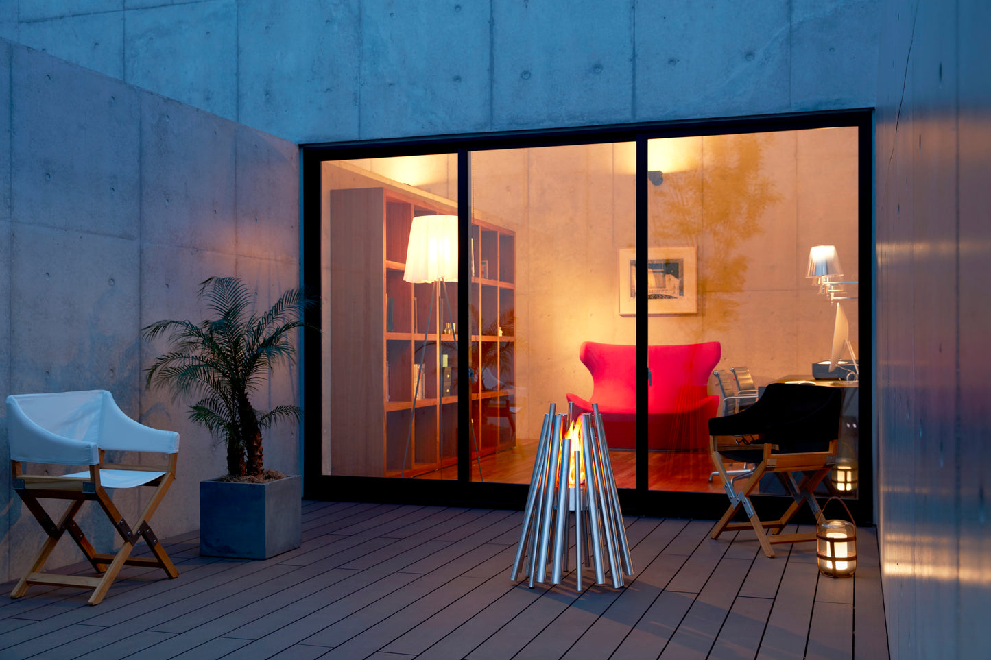 Modern outdoor patio with a fire pit, chairs, and a view into a home interior.