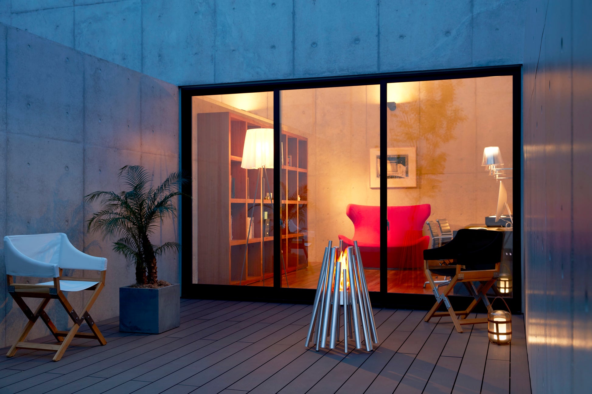 Modern outdoor patio with a fire pit, chairs, and a view into a home interior.