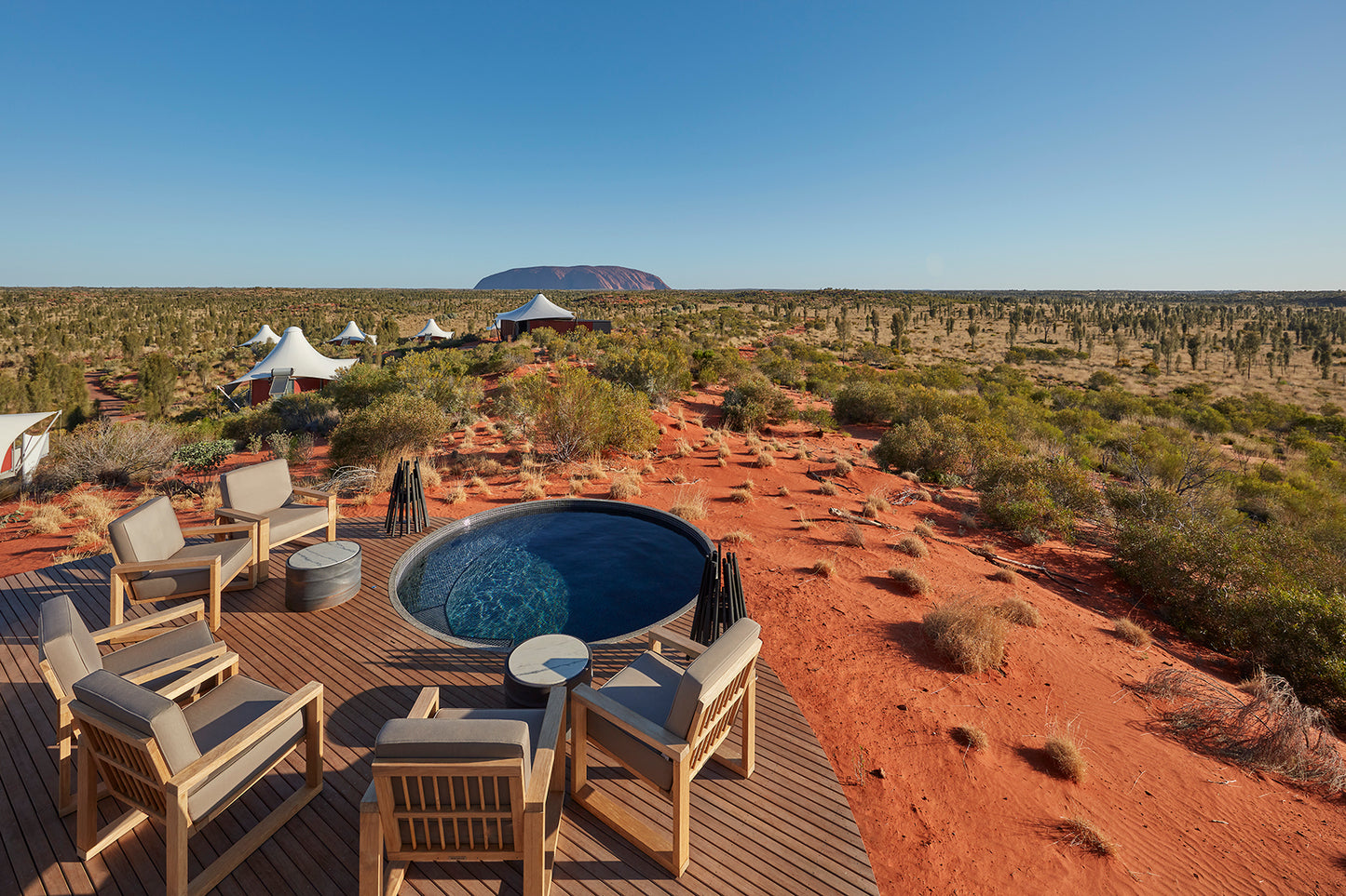 Outdoor seating area with a pool in the desert landscape, featuring Uluru in the background.