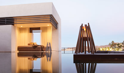 Modern outdoor setting with a bed and a lamp near a pool at dusk.