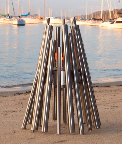 Metal fire pit on a beach with boats in the background